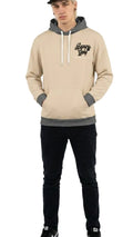 Person wearing a beige hoodie with gray accents and black pants on a white background