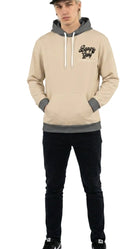 Person wearing a beige hoodie with gray accents and black pants on a white background