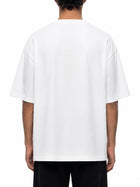 A person viewed from the back wearing an oversized white short-sleeve T-shirt and black pants against a plain white studio background.