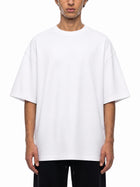 A model wearing an oversized white crewneck t-shirt with dropped shoulders, paired with black pants, shot against a plain white background.
