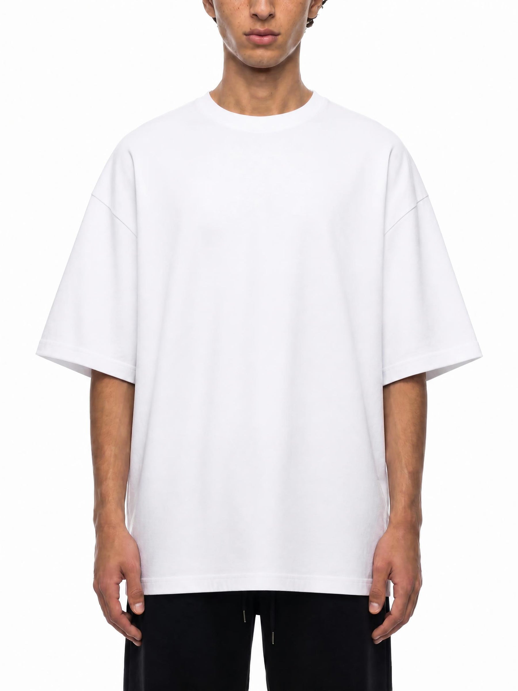 A model wearing an oversized white crewneck t-shirt with dropped shoulders, paired with black pants, shot against a plain white background.